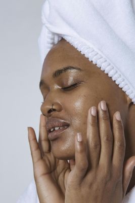 Side view of African American female with closed eyes in white turban massaging face against white background