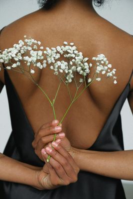Aesthetic back view of a woman holding white flowers against an elegant black dress.