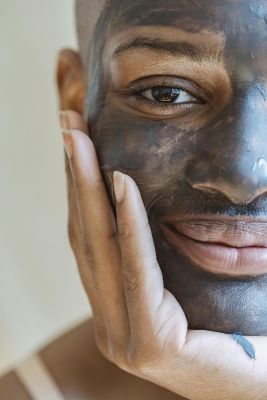 Close-up of a smiling woman applying a rejuvenating mud mask, showcasing skincare and beauty.