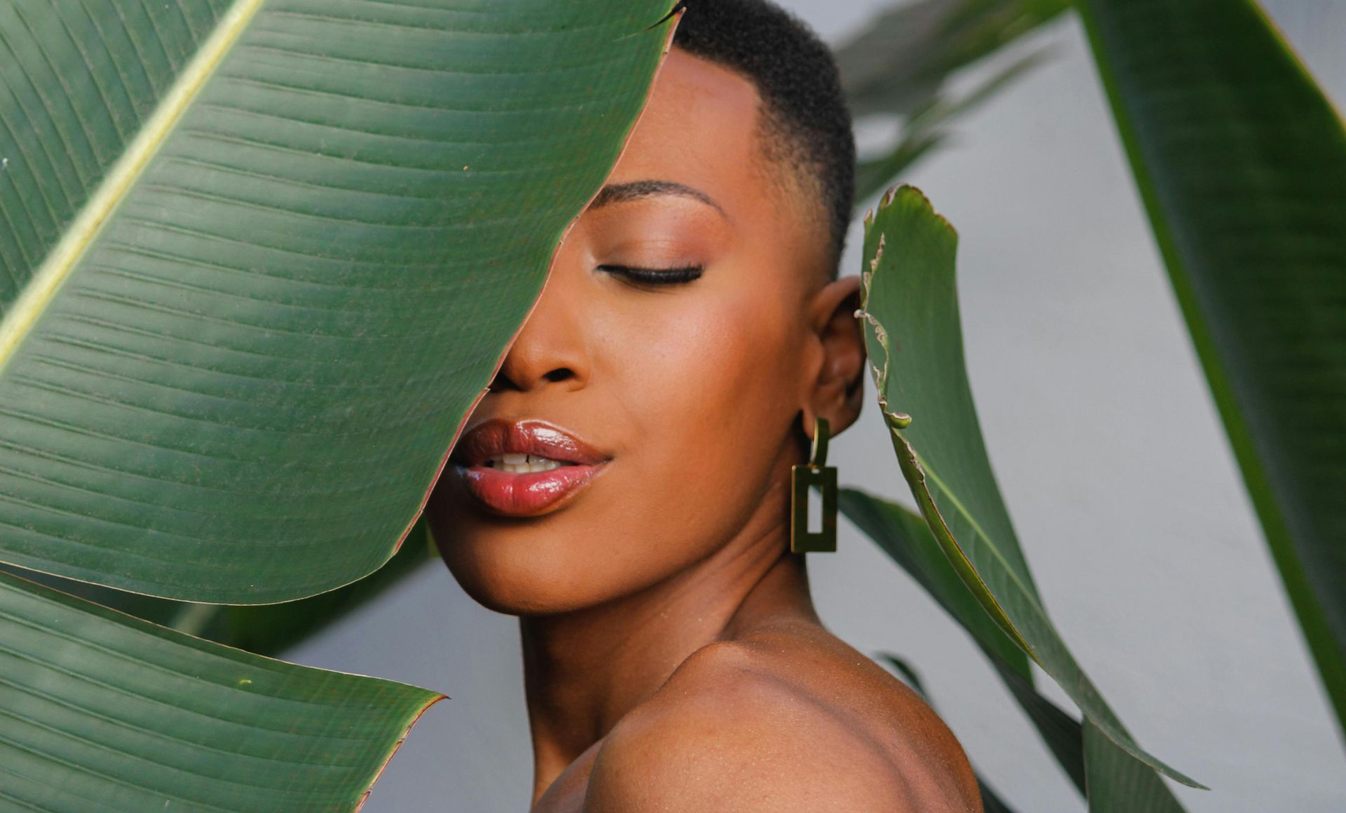 A serene portrait of a woman with closed eyes, framed by lush tropical leaves.