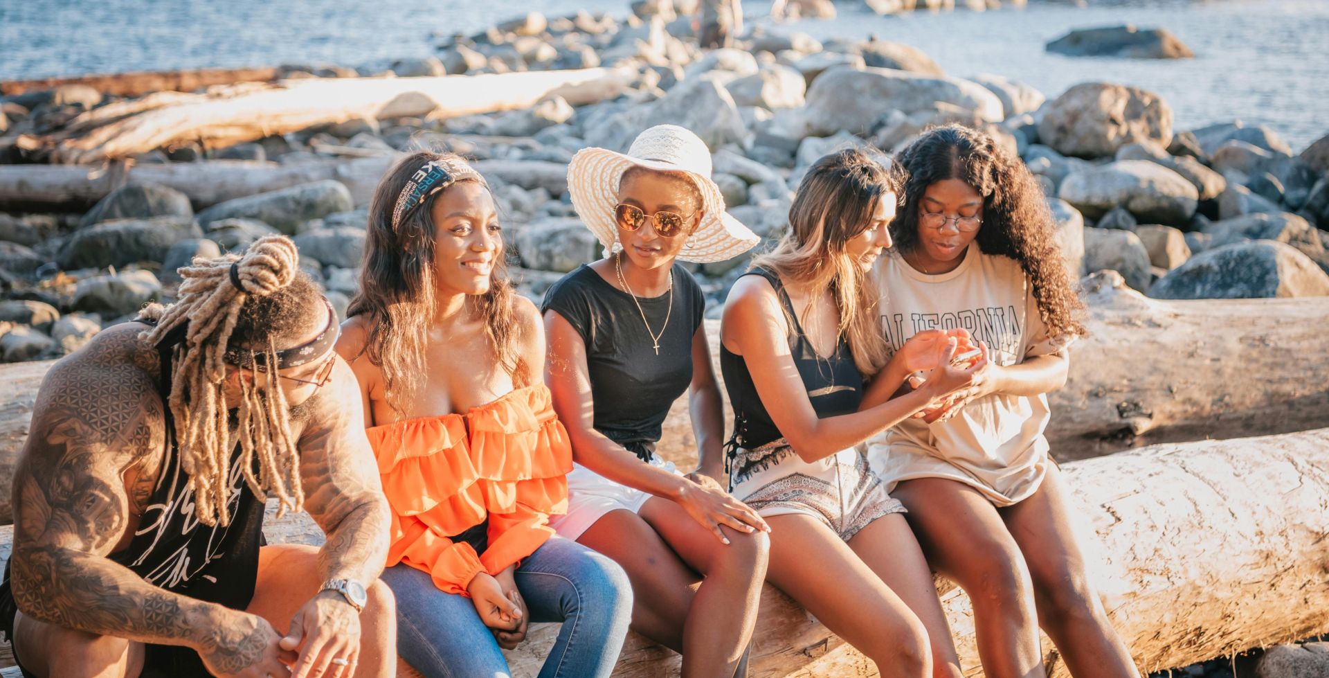 Five friends enjoying a sunny day by the rocky sea shore, sharing moments of relaxation and joy.